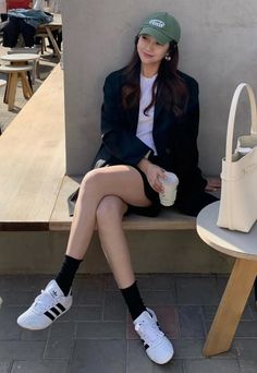 Woman in a green cap and black blazer sitting outdoors with a coffee cup