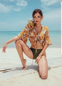 Woman in a bikini and floral top posing on a beach with an iguana on her shoulder