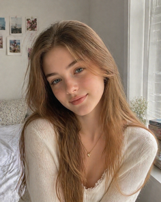 Young woman with long brown hair and blue eyes wearing a white top indoors