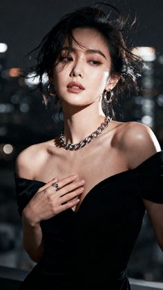 Woman in a black off-shoulder dress with a choker against a blurred cityscape at night