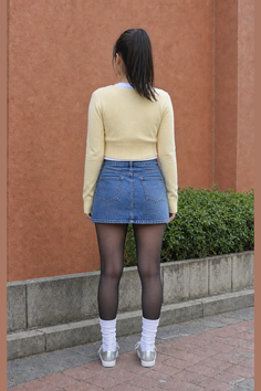 Woman with a ponytail wearing a denim skirt and black tights, seen from behind