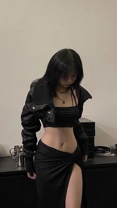 Woman with black hair wearing a black crop top and high-slit skirt indoors