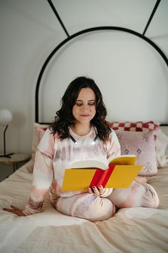 Woman in tie-dye pajamas reading a book with a neck light in a bedroom