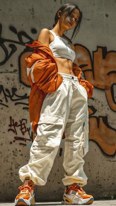Woman in a white crop top and cargo pants with an orange jacket against a graffiti wall