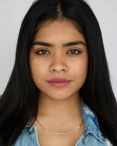 Woman with long black hair wearing a denim jacket and gold chain