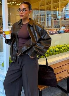 Woman in a leather jacket and glasses holding a coffee cup outside a bakery