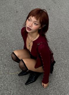 Woman with red hair and dark lipstick squatting outdoors