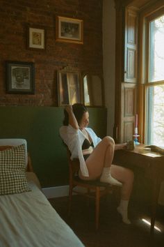 Woman in a bra and open white shirt sitting by a window in a warm-toned room