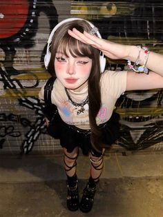 Person with long hair and headphones posing in front of a graffiti wall