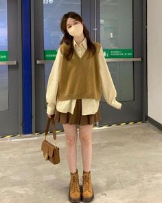 Woman in a brown vest and pleated skirt with a face mask and shoulder bag