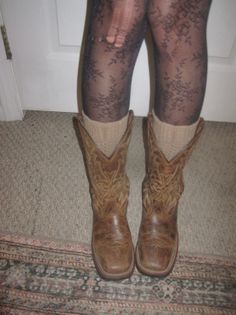 Legs wearing cowboy boots, beige socks, and torn lace tights indoors