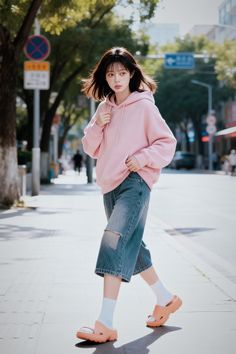Woman in a pink hoodie and ripped jeans walking on a sunny street