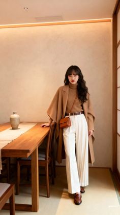 Woman in a brown turtleneck and white wide-leg pants with a brown coat indoors