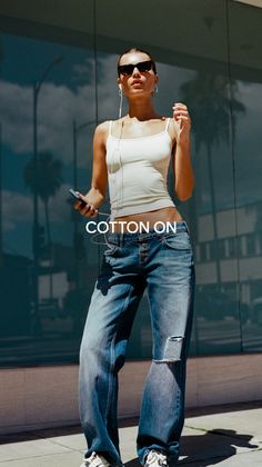 Woman in a white tank top and ripped jeans with sunglasses and earbuds outdoors