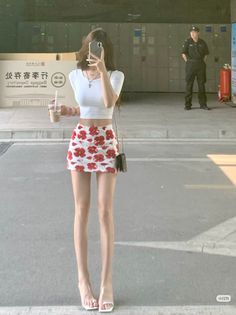 Woman in a white crop top and floral mini skirt holding a drink outdoors