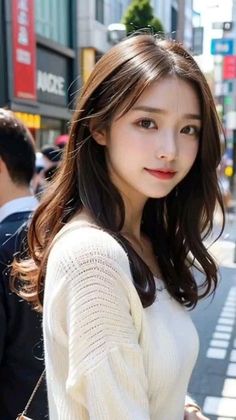 Woman with long brown hair wearing a white sweater on a city street