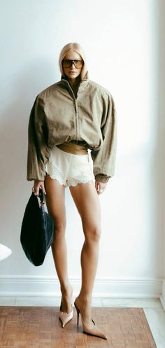 Woman in an oversized jacket, lace shorts, and high heels holding a black handbag