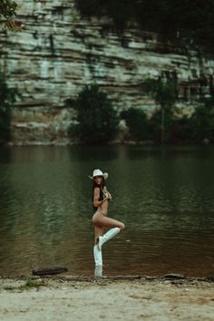 Woman in a cowboy hat and boots posing in a lake with a rocky cliff background
