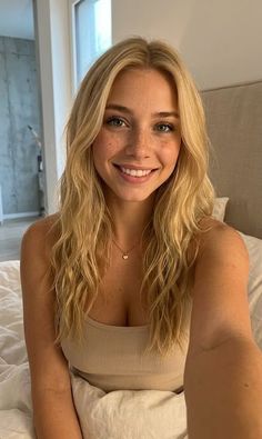 Blonde woman with freckles and long hair smiling in a tank top in a bedroom