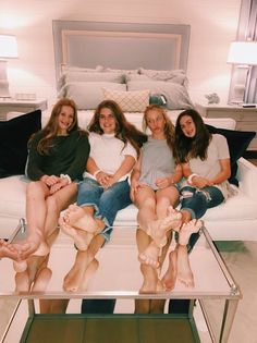 Four young women sitting on a white couch with their bare feet on a mirrored table