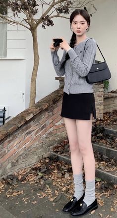Woman in a gray cardigan and black mini skirt holding a camera outdoors