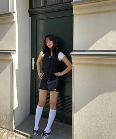 Woman in a black vest and mini skirt with white socks standing outdoors