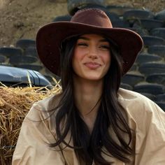Woman with long dark hair wearing a cowboy hat next to a hay bale