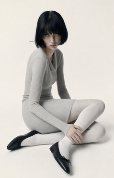 Woman with short black hair wearing a ribbed dress and white tights in a studio