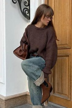 Woman in a brown sweater and blue jeans with a brown bag and boots