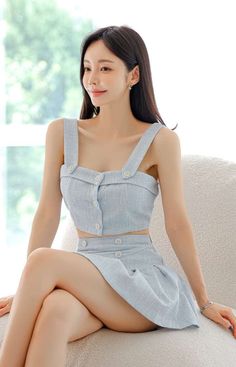 Woman in a light blue crop top and mini skirt sitting indoors