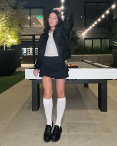 Woman in a black leather jacket and mini skirt standing outdoors at night