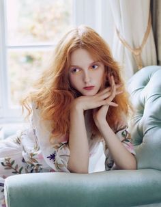 Woman with red hair and floral print top leaning on a light green sofa