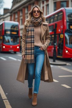 Woman in a trench coat and plaid scarf walking on a city street with red buses
