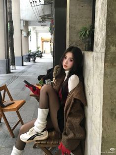 Woman with long dark hair wearing a brown coat and black tights at an outdoor cafe