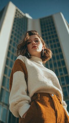Woman in a chunky sweater and high-waisted pants with a city building in the background