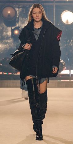 Woman with long blonde hair in an oversized black jacket and thigh-high boots
