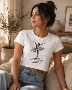 Woman in a white crop top with a ballet dancer graphic, sitting indoors