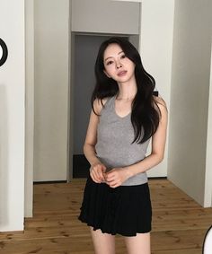 Woman with long dark hair wearing a grey tank top and black skirt indoors