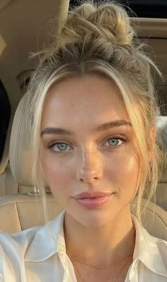 Woman with blonde hair in a messy bun, wearing a white shirt and necklace
