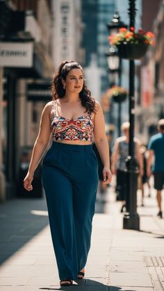 Woman in a patterned crop top and blue wide-leg pants walking on a street