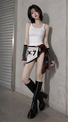 Woman in a white tank top and mini skirt with platform boots leaning against a wall