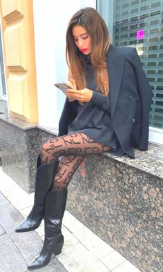 Woman in a black blazer and patterned tights sitting outdoors while looking at her phone