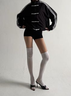 Person in a black jacket, short shorts, and thigh-high socks against a white wall