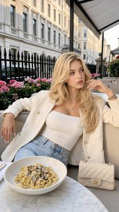 Blonde woman in a white jacket and jeans at an outdoor cafe