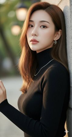 Woman with long brown hair wearing a black turtleneck and silver jewelry outdoors