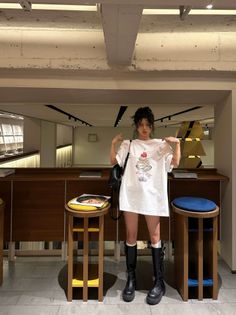 Woman in an oversized t-shirt and black boots posing indoors