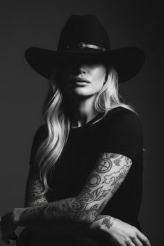 Woman in a cowboy hat with long blonde hair and arm tattoos in black and white