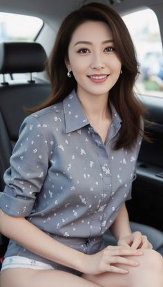 Woman with long hair and a grey patterned shirt smiling in a car