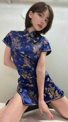 Woman in a blue cheongsam with dragon pattern and short hair posing indoors