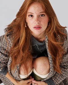 Woman with red hair and freckles wearing a plaid coat and gray sweater